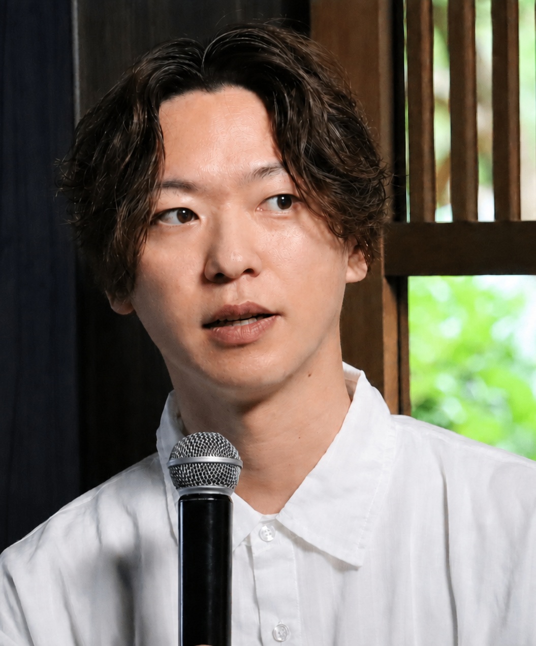 自然光の入る会場で、マイクを手に話す灰藤健吾
